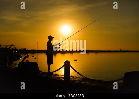 Un uomo che pesca nel pomeriggio alla baia Foto Stock