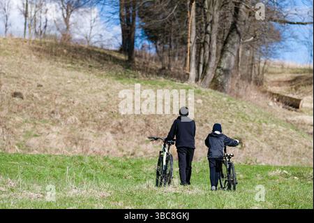 Due persone, forse padre e figlio, passeggiano lungo un sentiero erboso. Biciclette al traino. Tranquillo ambiente di campagna, bagnato dalla luce del sole. Colline e alberi Foto Stock