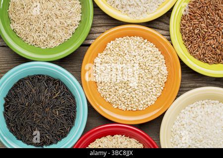 Una varietà di grani di riso su ciotole di ceramica colorata contro un legno a grana Foto Stock