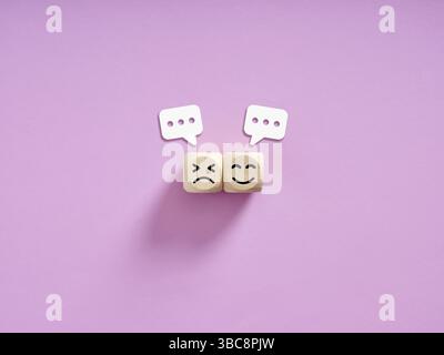 Due cubi di legno che mostrano un volto triste e un volto felice, con sopra delle bolle vocali, rappresentano il feedback e la soddisfazione del cliente Foto Stock
