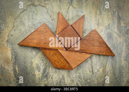 Immagine astratta di un pipistrello volante costruito con sette pezzi di legno tangram su uno sfondo di ardesia, Halloween Concept, opera d'arte creata dalla foto Foto Stock