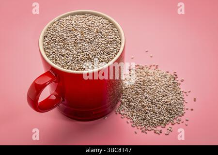 Una piccola tazza di caffè di semi di chia bianchi organici ricchi di acidi grassi omega-3 su sfondo rosa Foto Stock