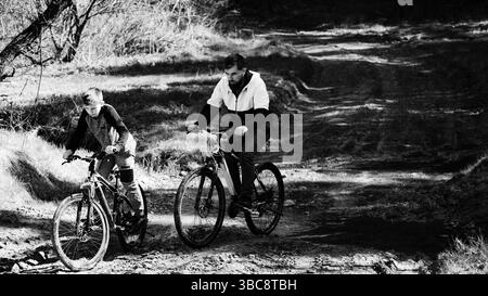 Un'immagine in bianco e nero cattura una scena emozionante di padre e figlio che pedalano insieme su un sentiero rustico. Il legame tra di loro è palpabile come loro Foto Stock