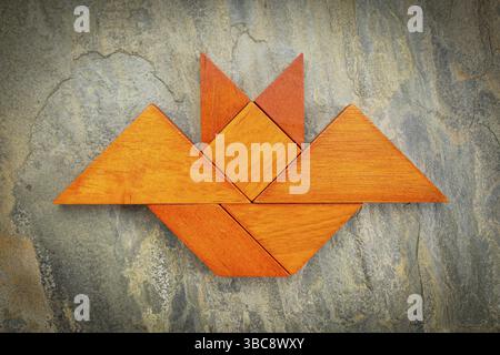Immagine astratta di un pipistrello volante costruito con sette pezzi di legno tangram su uno sfondo di ardesia, Halloween Concept, opera d'arte creata dalla foto Foto Stock