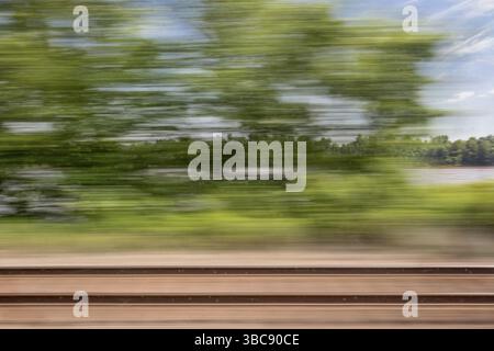 Sfocato paesaggio astratto di binari ferroviari e di un fiume visto dal finestrino del treno in movimento Foto Stock