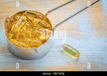 Capsule integratore di olio di pesce in un dosatore di metallo e legno grunge verniciato Foto Stock