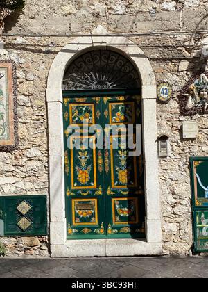 Tradizionale porta verde siciliana con decorazioni gialle di frutta e fiori, situata a Taormina, un'affascinante cittadina collinare sulla costa orientale di Sicil Foto Stock