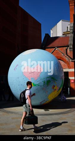 Un Hugh Globe del pianeta Terra in una strada stretta con giovani che camminano nella City di Londra, in Inghilterra Foto Stock