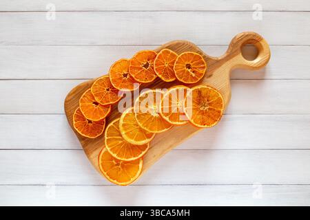Fette di arancia secca e mandarino disposte in due file ordinate su un tagliere di legno posto su un tavolo di legno bianco Foto Stock