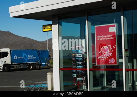 Akranes, Islanda - 16 maggio 2025: Un camion blu vicino a un moderno edificio in vetro ad Akranes, Islanda, con cieli limpidi. Foto Stock