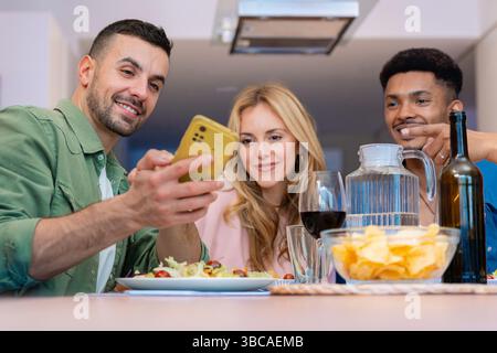 Amici multietnici felici gustando spuntini e bevande in una cucina moderna e luminosa Foto Stock
