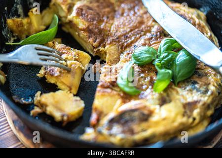 Tradizionale tortilla di patate spagnola per colazione in una padella di ghisa. Tagliare a pezzi con un coltello e una forchetta. Foto di alta qualità Foto Stock