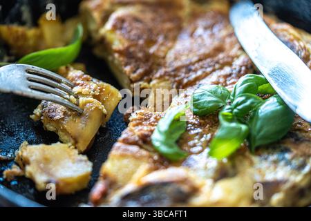 Tradizionale tortilla di patate spagnola per colazione in una padella di ghisa. Tagliare a pezzi con un coltello e una forchetta. Foto di alta qualità Foto Stock
