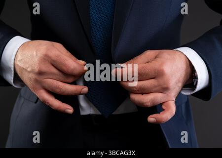 Primo piano delle mani di un uomo d'affari che abbelliscono la sua tuta blu navy, sottolineando l'eleganza e lo stile professionale. Foto Stock