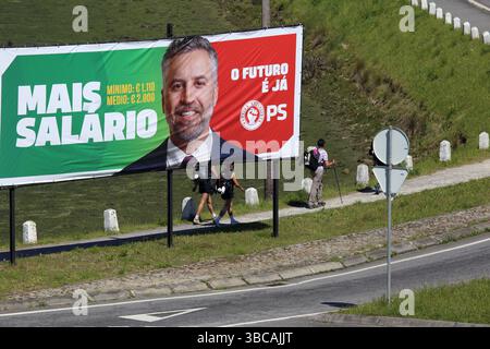 Viana do Castelo, Portogallo - 15 maggio 2025: I pellegrini passano davanti a un cartellone della campagna del Partito Socialista che promuove l'aumento dei salari prima del giorno delle elezioni Foto Stock