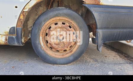 Primo piano di una ruota arrugginita e di un parafango su un'auto abbandonata, evidenziando gli effetti degli agenti atmosferici e dell'abbandono sul veicolo parcheggiato sulla strada Foto Stock