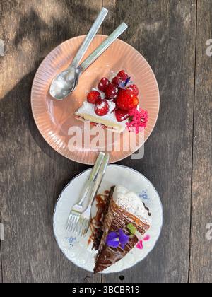 Due fette di torta sui piatti: Shortcake alle fragole e torta al caramello al cioccolato con panna montata, servita su un rustico tavolo di legno. Foto Stock