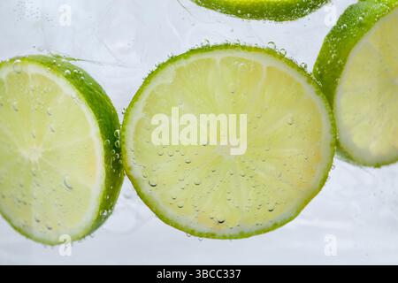Rinfrescante acqua soda con fette di lime e ghiaccio in vetro su sfondo bianco, primo piano Foto Stock