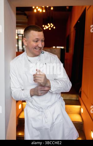 cuoco caucasico sorridente pronto a cucinare in cucina, con grembiule bianco. Foto Stock