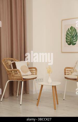 Soggiorno con tenda a finestra color pastello, tavolo in legno e sedie in rattan Foto Stock