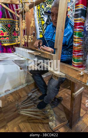 Un artigiano Bukhara in Uzbekistan lavora su un telaio tradizionale, tessendo tessuti colorati che riflettono secoli di patrimonio artigianale locale. Foto Stock