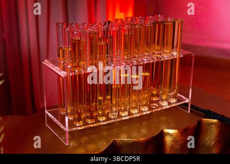 Provette multiple riempite con una bevanda di colore dorato disposte in un rack trasparente, illuminato da un'illuminazione rossa. Foto Stock