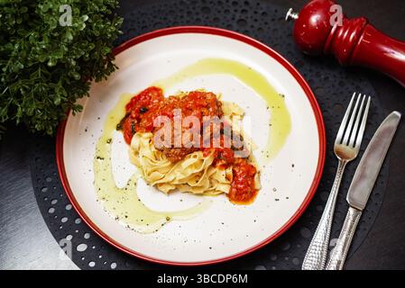 Deliziose tagliatelle condite con polpette succose in una ricca salsa di pomodoro, guarnite con olio d'oliva e pepe nero. Foto Stock