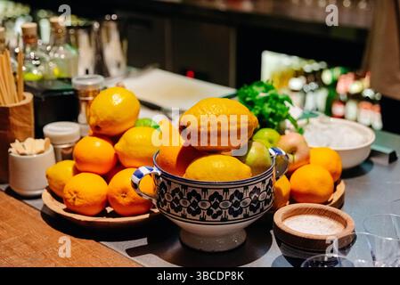 Limoni assortiti, arance e limoni disposti in ciotole di ceramica e vassoi di legno su un bancone del bar con illuminazione soffusa. Foto Stock