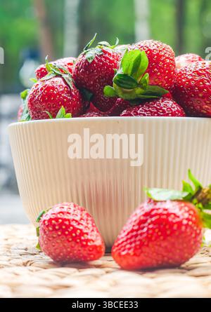 Bowl filled with ripe strawberries on woven mat with soft green background ambiance. High quality photo Foto Stock