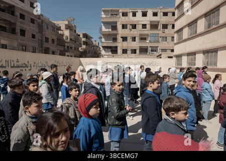 20 maggio 2025, Damasco, Siria: DAMASCO, SIRIA - 15 APRILE: Gli studenti eseguono un saluto mattutino nel parco giochi ristrutturato della scuola mista Zamalka il 15 aprile 2025 a Jobar, Damasco, Siria. La bandiera a tre strisce si riferisce al nuovo regime. Tutte le pareti della scuola sono state recentemente dipinte per rimuovere riferimenti visivi all'ex presidente siriano Bashar al-Assad.Jobar, un sobborgo della capitale siriana Damasco, è stato per anni un fronte strategico nella guerra civile e una sede per le ex milizie Hay'at Tahrir al-Sham. Con l'aiuto della Russia, il sobborgo è stato distrutto dall'ex presidente siriano Bashar A. Foto Stock