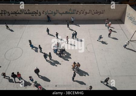 20 maggio 2025, Damasco, Siria: DAMASCO, SIRIA - 15 APRILE: Gli studenti giocano nel parco giochi rinnovato della scuola mista Zamalka il 15 aprile 2025 a Jobar, Damasco, Siria. La bandiera a tre strisce si riferisce al nuovo regime. Tutte le pareti della scuola sono state recentemente dipinte per rimuovere riferimenti visivi all'ex presidente siriano Bashar al-Assad.Jobar, un sobborgo della capitale siriana Damasco, è stato per anni un fronte strategico nella guerra civile e una sede per le ex milizie Hay'at Tahrir al-Sham. Con l'aiuto della Russia, il sobborgo è stato distrutto dall'ex presidente siriano Bashar All-Assad. (Credito immag Foto Stock