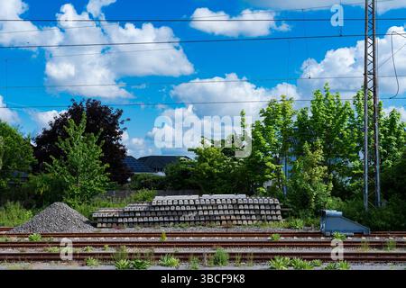 Le traversine in cemento sono impilate ordinatamente accanto ai binari ferroviari, adagiate su uno sfondo di lussureggianti alberi verdi e un cielo blu luminoso con soffici nuvole. Foto Stock