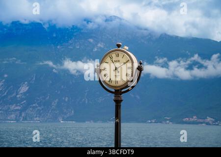 Attracco barche a Limone sul Garda, Lago di Garda, Italia, con grande orologio classico. Monte Baldo sullo sfondo, avvolto nelle nuvole Foto Stock