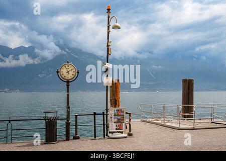Attracco barche a Limone sul Garda, Lago di Garda, Italia, con grande orologio classico. Monte Baldo sullo sfondo, avvolto nelle nuvole Foto Stock