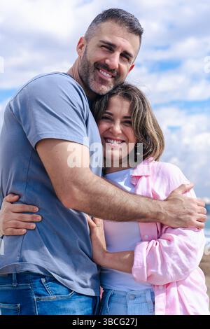 Ritratto di coppia caucasica in vacanza al mare abbracciato con l'oceano sullo sfondo. Verticale Foto Stock
