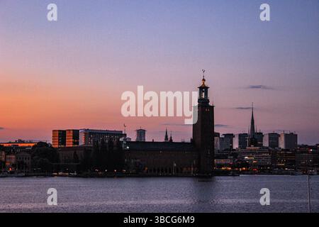 Il municipio di Stoccolma (Stadshuset) si staglia su un cielo color pastello al tramonto, con la guglia della chiesa di Klara e gli edifici moderni sullo sfondo Foto Stock