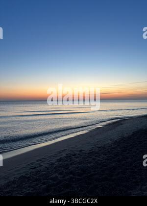Una scenografia minimalista del tramonto sulla costa del Mar Baltico. La foto cattura una costa tranquilla con onde dolci e morbide sfumature pastello nel cielo Foto Stock