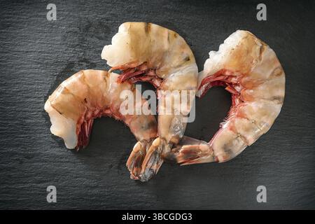 Tre gamberi giganti crudi di tigre, puliti, senza testa e pronti per cucinare su un piatto di ardesia scura, vista dall'alto, messa a fuoco selezionata Foto Stock