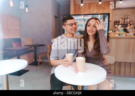 Giovani coppie che si godono un caffè insieme in un caffè moderno durante il giorno, condividendo sorrisi e risate Foto Stock