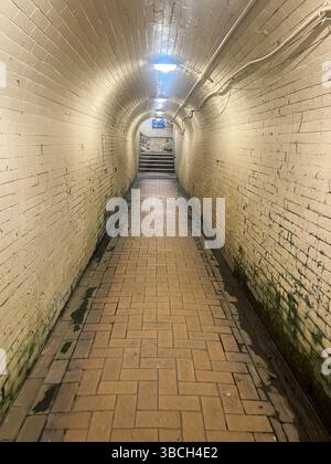 Un lungo e stretto tunnel in mattoni con pavimento in mattoni. Il tunnel è buio e vuoto. Non ci sono persone o oggetti visibili nel tunnel Foto Stock