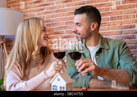 Coppia caucasica che festeggia la nuova casa con vino rosso e sorride l'una all'altra Foto Stock