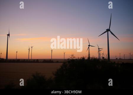 Le turbine eoliche si stagliano contro un tramonto colorato su un tranquillo paesaggio aperto, la Germania Foto Stock