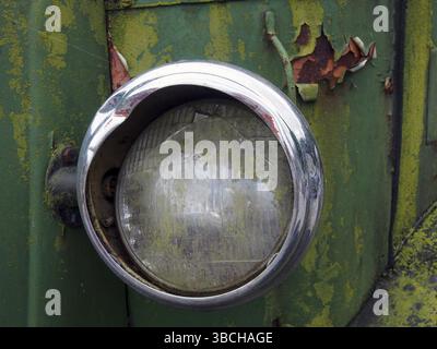 Primo piano del faro rotto di un vecchio camion abbandonato con vernice verde arrugginita Foto Stock