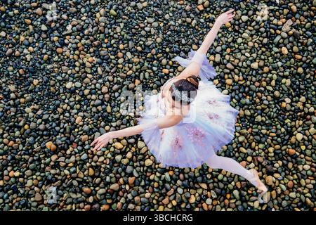 La ballerina in un tutù bianco posa graziosamente su una spiaggia ricoperta di ciottoli. WASHINGTON, STATI UNITI Foto Stock