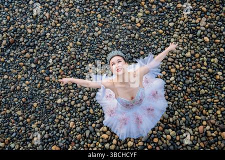 Ballerina in tutù posa gioiosamente con le braccia allungate su una spiaggia di ciottoli. WASHINGTON, STATI UNITI Foto Stock