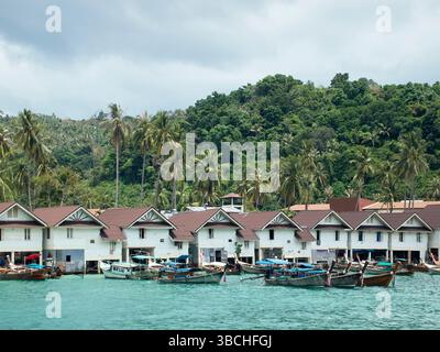 Case sul lungomare con barche attraccate, circondate da lussureggianti palme e densa foresta verde. Thailandia Foto Stock