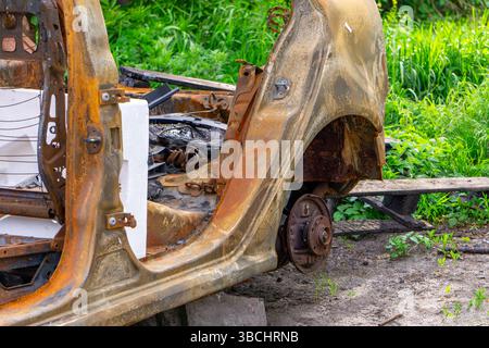 Guscio arrugginito di un'auto bruciata senza porte o ruote, posto a terra circondato da erba. Foto Stock