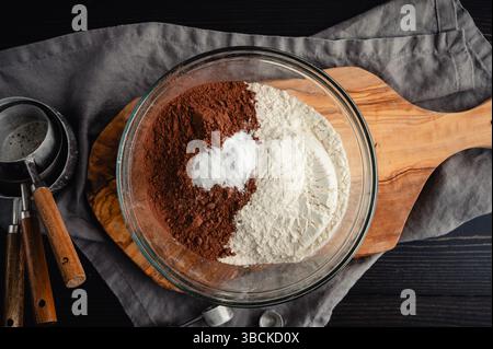 Ingredienti secchi per biscotti al cioccolato nel recipiente di vetro: Vista dall'alto del cacao in polvere, della farina multiuso, del bicarbonato e del sale Foto Stock