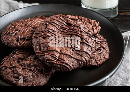 Primo piano del piatto di biscotti alla ciliegia al cioccolato con bicchiere di latte: Dessert con biscotti alla ciliegia al cioccolato impilato su un piatto con una tazza di latte Foto Stock