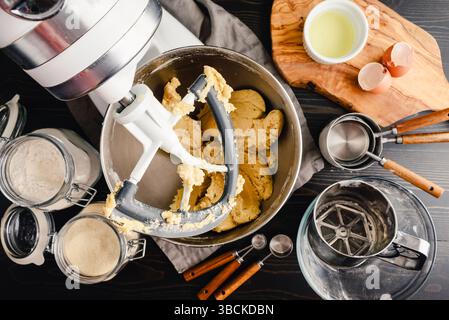 Preparazione dell'impasto per biscotti allo zucchero in un mixer da tavolo: Vista dall'alto di un mixer da tavolo con attacco a paletta e circondato da ingredienti e attrezzature Foto Stock